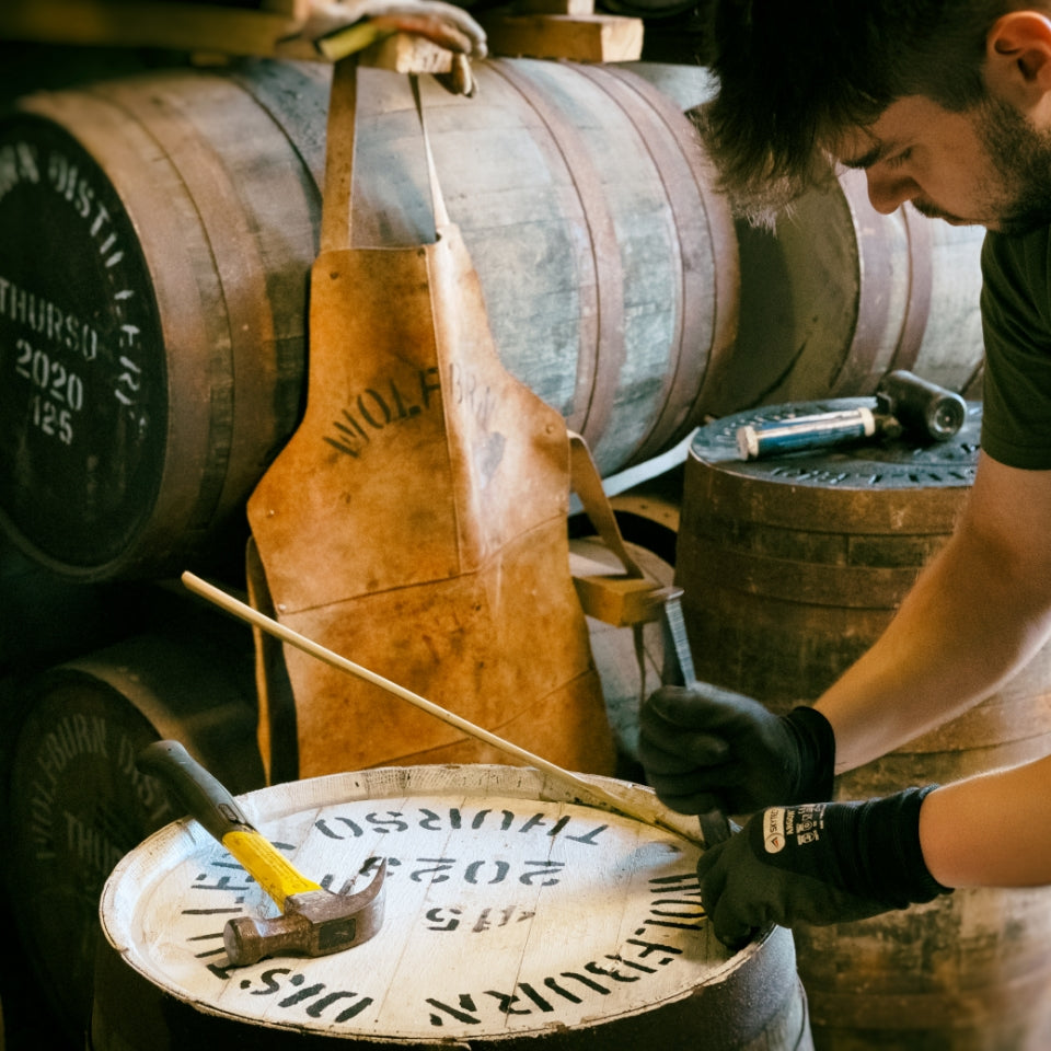 Person working with barrels in a whisky distillery setting