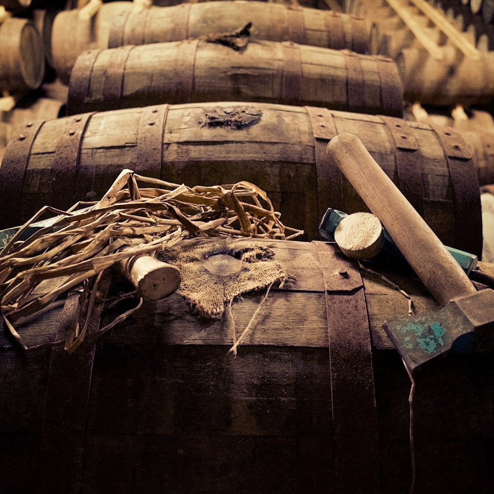 Close-up of wooden barrels with creeds and a cask hammer and bung in a warehouse setting.