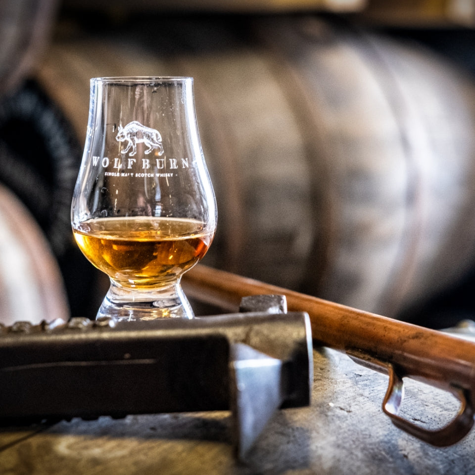 Glass of whiskey with Wolfburn branding on a wooden barrel background