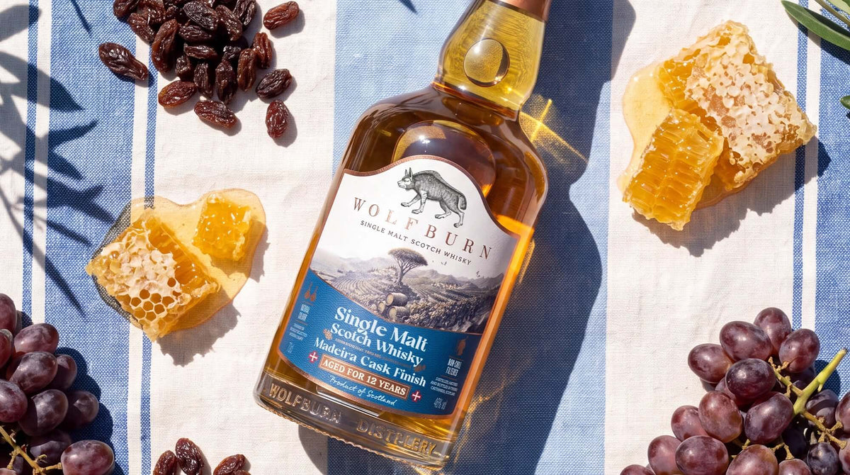 Wolfburn 12 Year Old Madeira Cask Finish bottle on striped linen with raisins, honeycomb and dark grapes