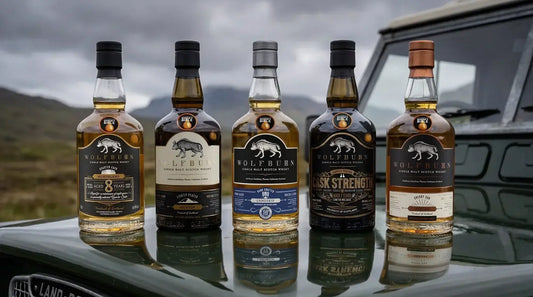 Five bottles of Wolfburn whisky on a Old Land Rover bonnet with a scenic Highland background