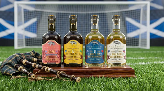 Four Wolfburn 2026 Scotland World Cup Edition limited edition single malt whiskies — Campaign Bottle, 12 Year, 8 Year and 10 Year — displayed on a wooden stand on football pitch turf with Scottish bagpipes and tartan in the foreground