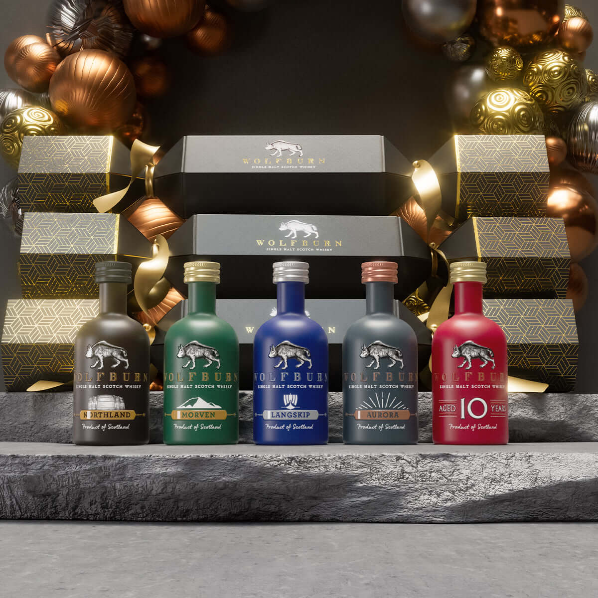 A set of miniature whisky Christmas crackers with baubles on a stone plinth 
