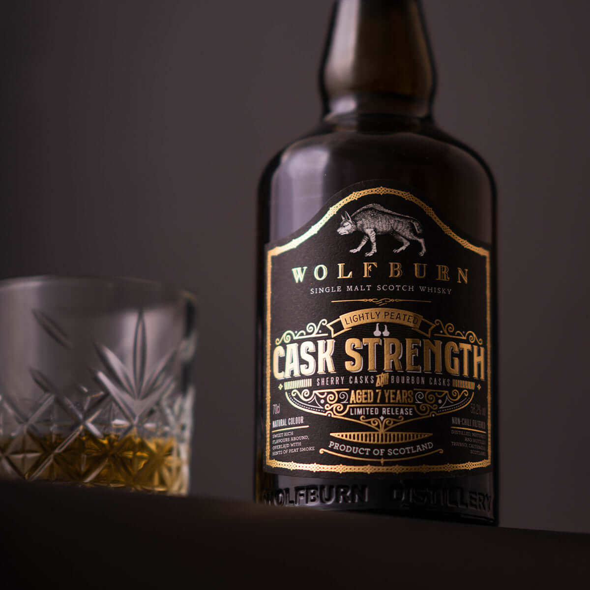 Bottle of Wolfburn Cask Strength Single Malt Whisky with a glass, showing its unique branding and color.
