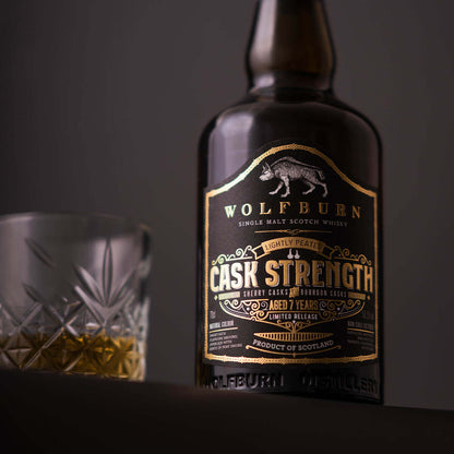 Bottle of Wolfburn Cask Strength Single Malt Whisky with a glass, showing its unique branding and color.