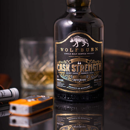 Wolfburn Cask Strength whisky bottle with a glass of whisky in the background