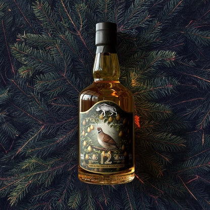 Bottle of whisky with a label featuring a partridge design on a dark background with pine branches.