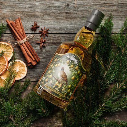 Bottle of Wolfburn whisky with a partridge label on a wooden surface with cinnamon sticks and oranges.