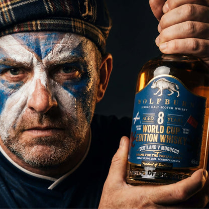 Scottish man with face painted in blue and white holding a bottle of Wolfburn Single Malt Scotch Whisky.