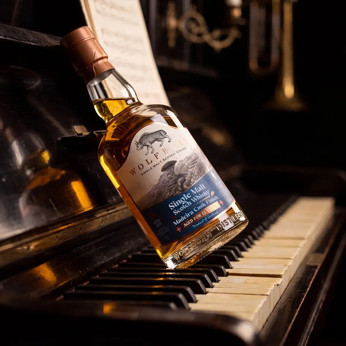 Wolfburn 12 Year Old Madeira Cask Finish bottle resting on the keys of an old piano with sheet music behind