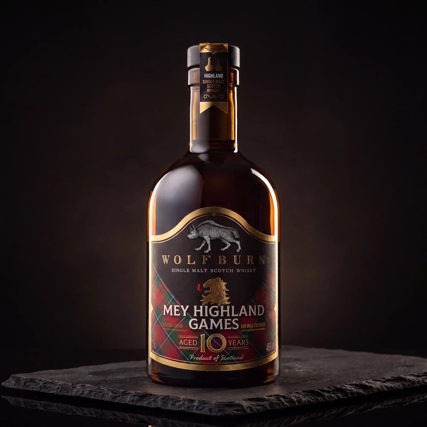 A bottle of Wolfburn 'Mey Highland Games' aged 10 years single malt Scotch whisky, presented on a dark slate slab against a dark studio background.