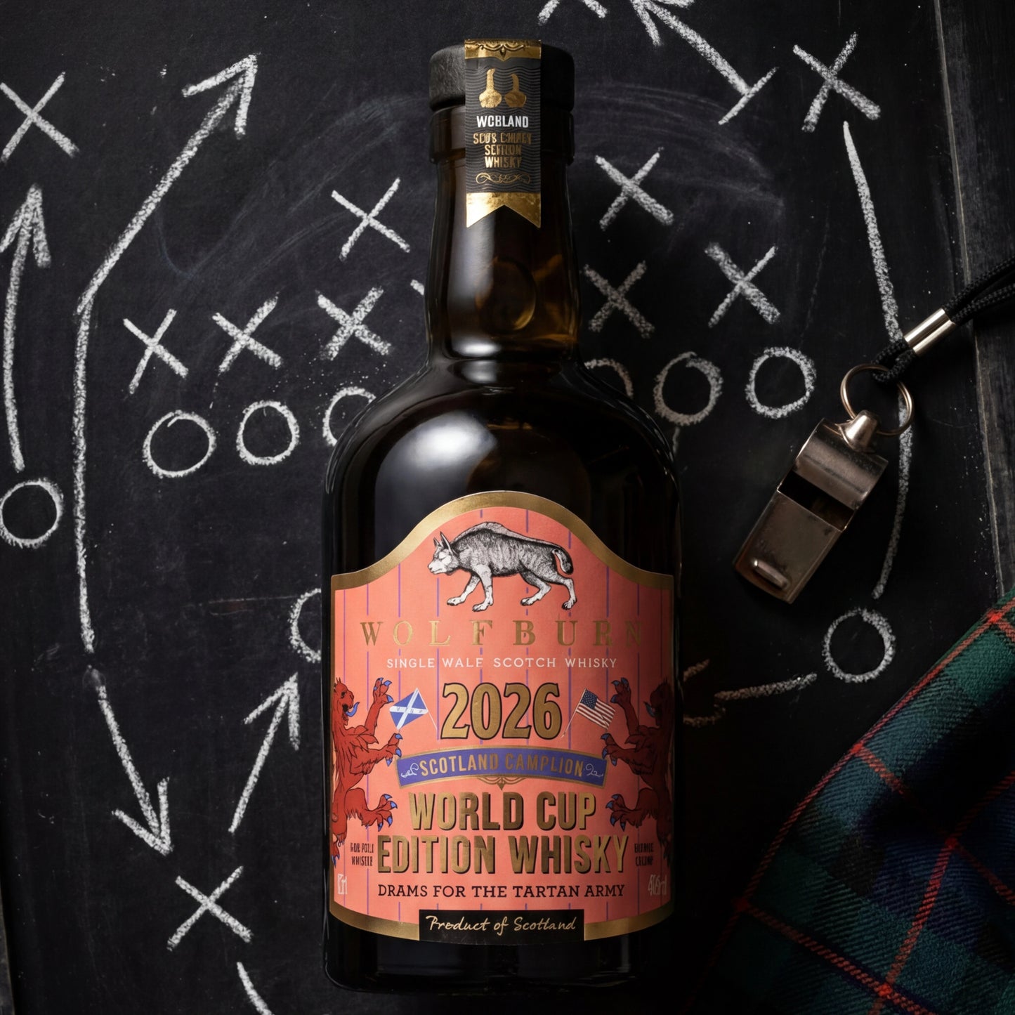 Wolfburn Morven World Cup Edition 2026 Highland Single Malt Scotch Whisky bottle on football tactics chalkboard with referee's whistle and tartan scarf, coral pinstripe label with Saltire and US flag