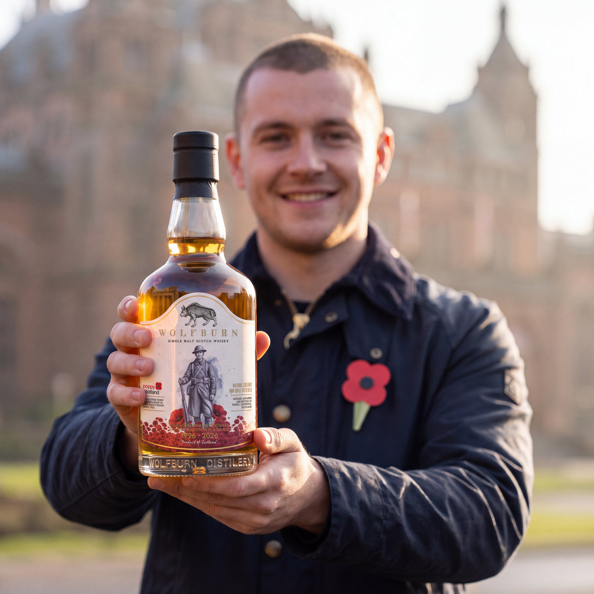 Smiling supporter wearing a Scottish poppy holds up the Wolfburn Poppyscotland 12 Year Old single malt Scotch whisky