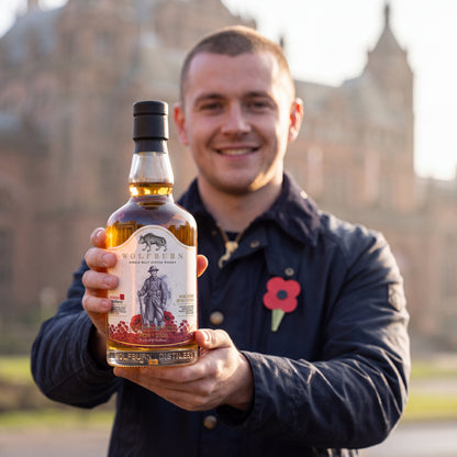 Smiling supporter wearing a Scottish poppy holds up the Wolfburn Poppyscotland 12 Year Old single malt Scotch whisky